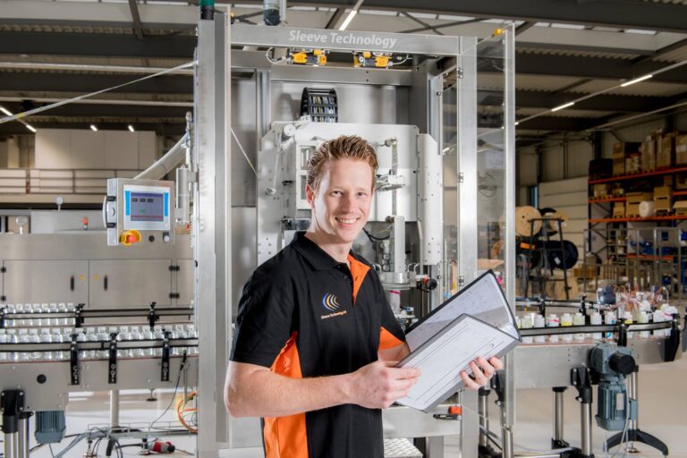 Sleeve Technology support engineer reviewing documentation in front of a sleeve application machine